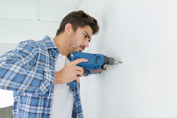 male builder drilling holes in wall at construction site