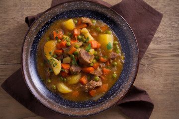 Stew, made with beef,  potatoes, carrots and green peas. Goulash soup in a bowl on wooden table. overhead, horizontal