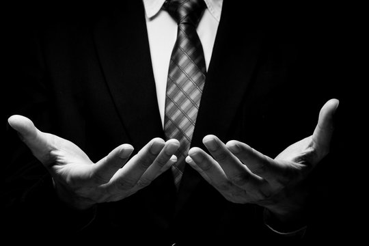 Close up of man in black suit with hand gesture on black background. black and white tone - Powered by Adobe