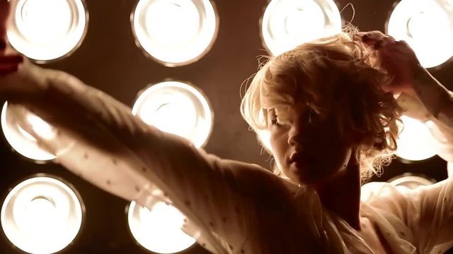 Young female blonde caucasian dancer dancing in front of studio light. Closeup shot.
