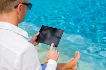 Businessman with tablet sitting by the pool