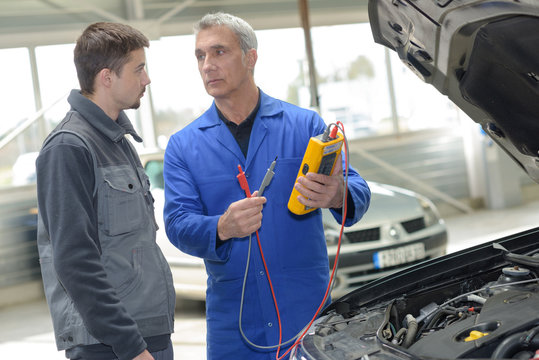 two mechanics looking at and working on a car