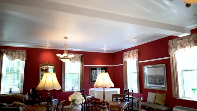 Camera starts on an antique ceiling light and angles down to reveal two women talking in a beautiful red lounge room while sitting on couches.