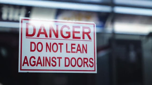 Warning sign saying Do Not Lean Against Doors on moving subway