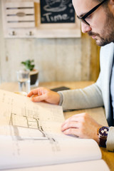 Young architect looking over building plans while he's on a break in a modern cafe.