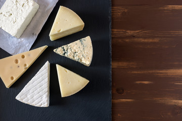Different kinds of cheeses on black stone board.
