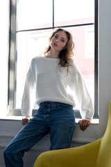 Fototapeta premium portrait of beautiful young brunette woman sitting in windowsill and looking at camera