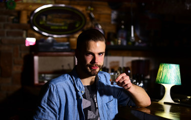 Man with beard drinks alcohol in bar on blurred background.