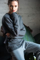 portrait of beautiful brunette woman in fashionable outfit sitting on armchair and looking at camera