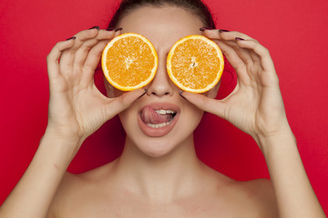 Happy sexy woman posing with slices of orange on her face on red background