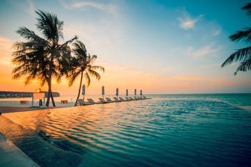 Luxury pool and beach in sunset - palm trees and sun umbrellas and loungers. Luxury beach background