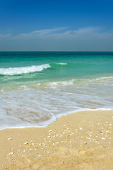 Amazing beach with turquoise ocean, white small waves hitting golden beach somewhere in Dubai.
