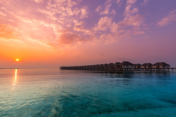 Sunset in Maldives island. Beautiful sunset sky and clouds, luxury water villas and wooden pathway...