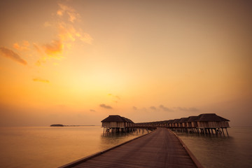Fototapeta premium Sunset in Maldives island. Beautiful sunset sky and clouds, luxury water villas and wooden pathway - pier