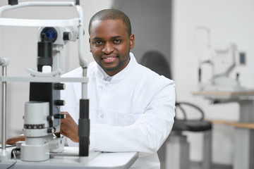 Young man standing near medical equipment for vision checking and improving. Looking friendly and ready for therapy. Wearing white classic shirt.