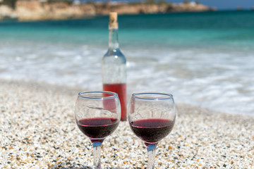Glasses of red wine and bottle on the beach at the summer sunny day. Sea on the background.