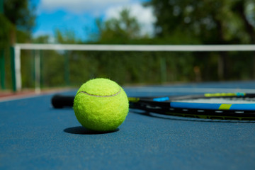 Close up of yellow ball is on tennis racket background, laying on blue tennis court carpet. Photo of professional sport equipment. Concept of tennis outfit photografing.