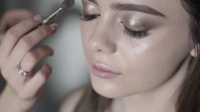 Makeup artist to apply highlighter. Young girl doing professional makeup