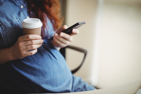 Pregnant businesswoman using mobile phone while having coffee
