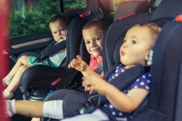 Three children in car safety seat - family, transport, safety, road trip and people concept