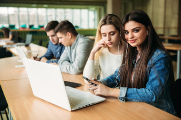 Group of college students studying in the school library, a girl and a boy are using a laptop and connecting to internet