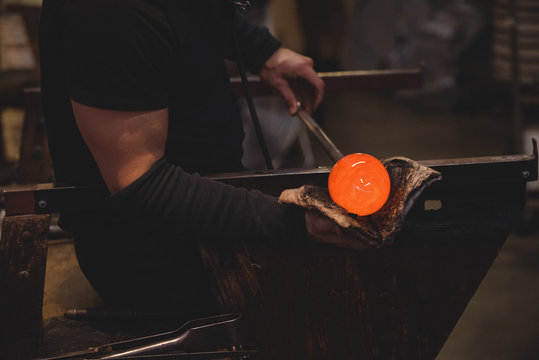 Glassblower shaping molten glass piece with a wet cloth