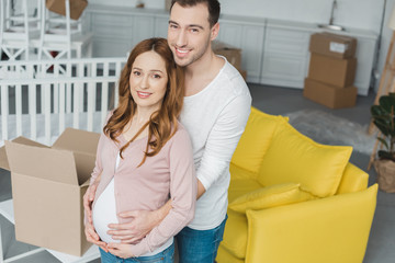 high angle view of happy pregnant couple smiling at camera in new apartment