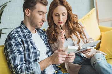 young couple taking notes and using calculator during relocation