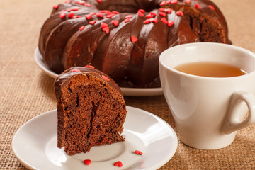Slice of delicious homemade chocolate cake decorated with small hearts made of caramel on saucer and cup of tea on table with sackcloth