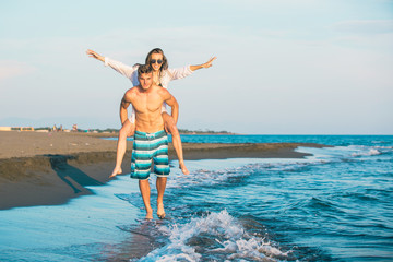 Happy couple in love on beach summer vacations. Joyful girl piggybacking on young boyfriend  having fun.