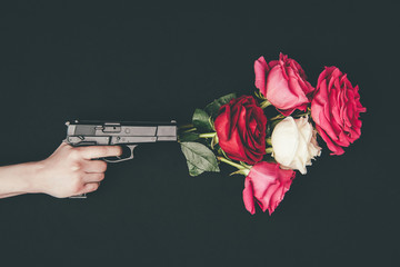 Female hand holding gun with bouquet of rose flowers isolated on black