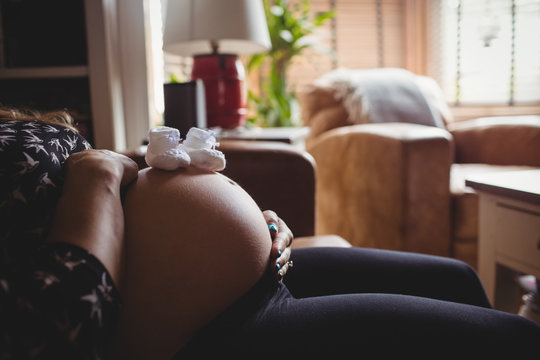 Pair of baby socks on pregnant woman stomach in living room