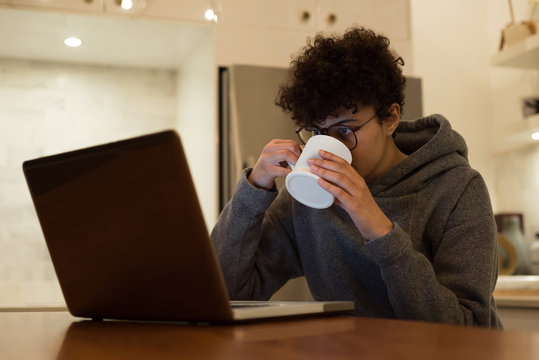 Woman using laptop while having coffee in kitchen