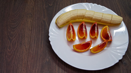pieces of blood orange and banana on a white plate, top view