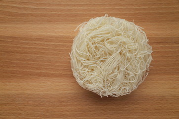 A nest of dried rice noodles for soups and stir fries photographed from above on a wooden chopping...