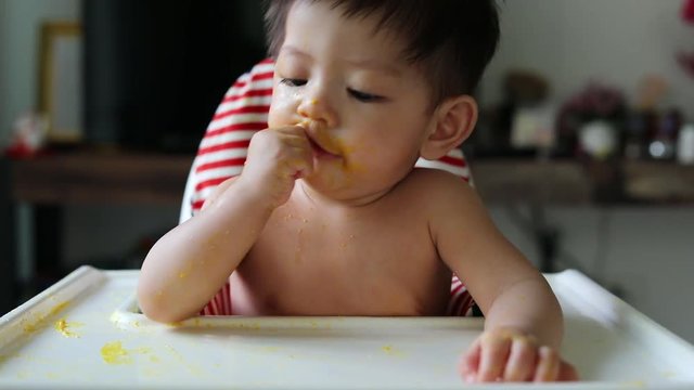 slow-motion, cute baby using finger hand in mouth itchy gum first primary tooth teething with food puree dirty on face
