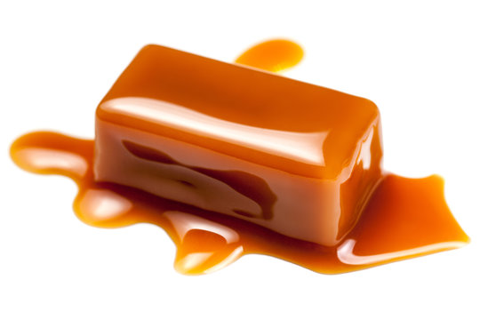 Caramel sauce flowing on caramel candies, isolated on white background. Golden Butterscotch toffee candy caramels.