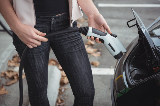 Mid section of woman charging electric car