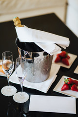 Bottle of champagne in bucket with ice and empty glasses on black table with delicious strawberry. Served table with dessert and alcoholic drink for special occasion