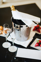 Vertical shot of bottle with alcoholic drink in busket to be cooler, two glasses and dessert for celebration something. Tasty juicy strawberry and champagne. Celebration.