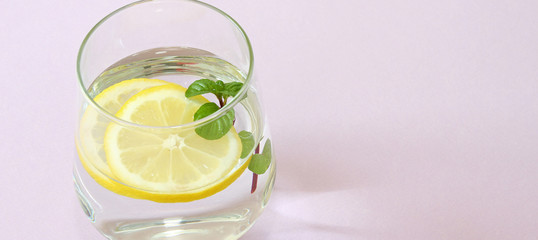 Glass of water, lemon and mint. Glass of pure water and fresh organic lemon and mint isolated on purple background. Detox and healthy food concept.