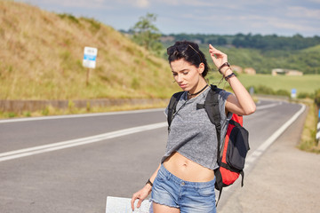 women with paper map waving at car on a concrete road in the countryside.