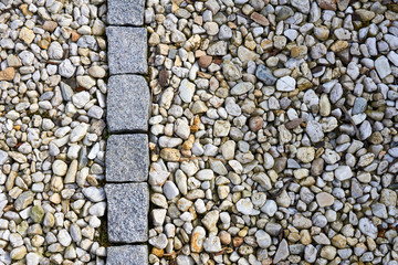 Old gray paving stones in a row surrounded by pebbles