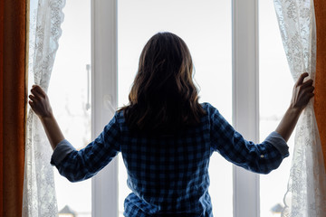 The silhouette of a young woman reveals the curtains at the panoramic window