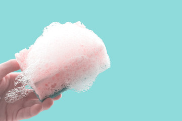 Female hand cleaning window with yellow sponge and detergent on blue background. Soap stains on the glass. Home Cleaning concept.