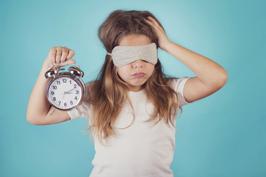 ni&ntilde;a peque&ntilde;a con un reloj despertador sobre fondo azul
