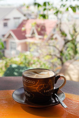 Cup with hot milk coffee on a colorful wooden table in a cafe on background of city view. Dalat, Vietnam.