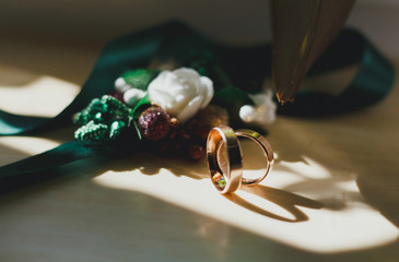 Golden rings in the sun lights on the table. Wedding details with dark green buttonhole on...