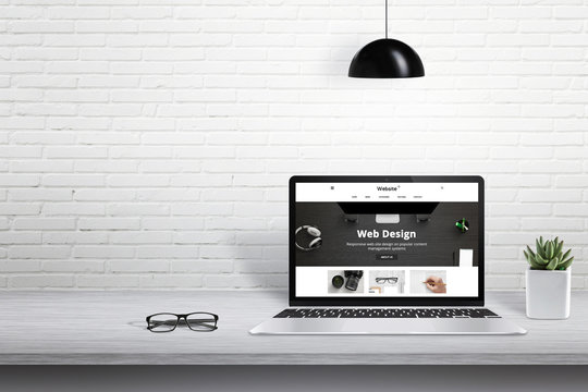 Laptop with modern web site presentation. Free space for text beside on white brick wall.