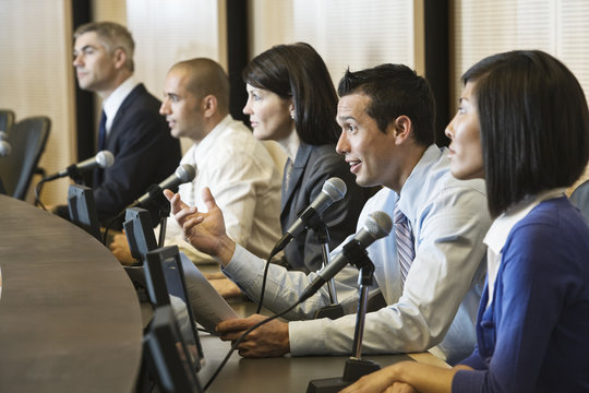 A political meeting with a mixed race group of people at microphones.